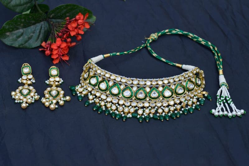 A kundan choker and matching earrings with green enamel drops on dark blue cloth