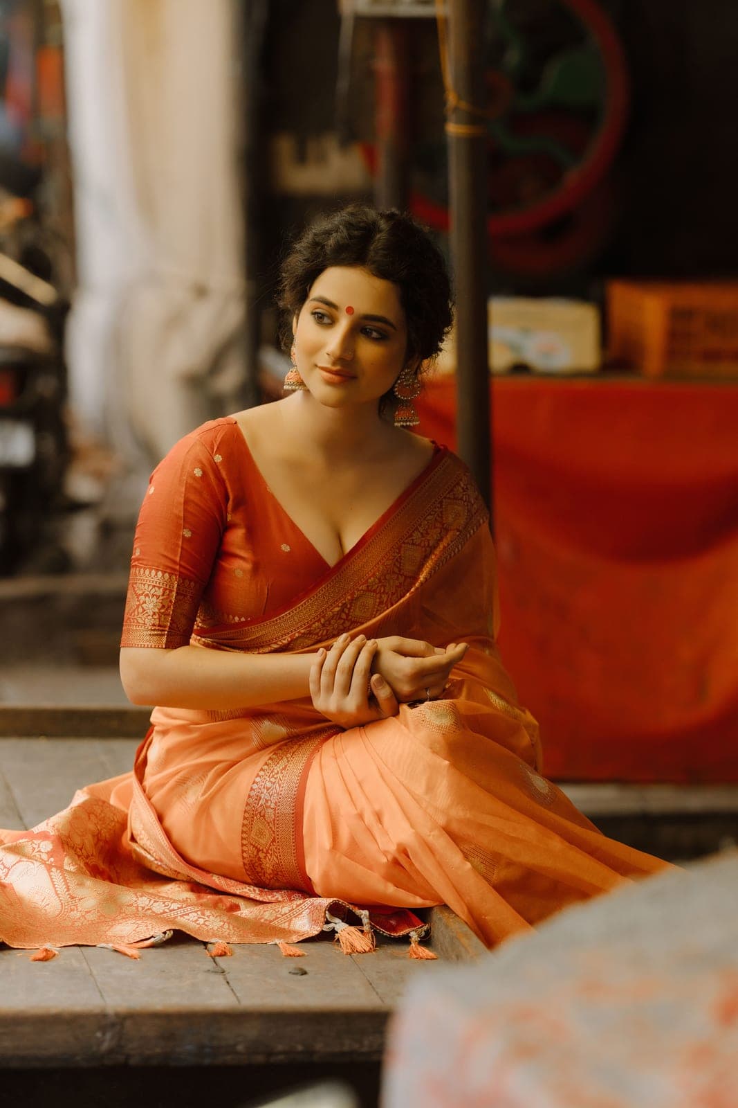 The model seated on a shop step in a saffron Banarasi saree
