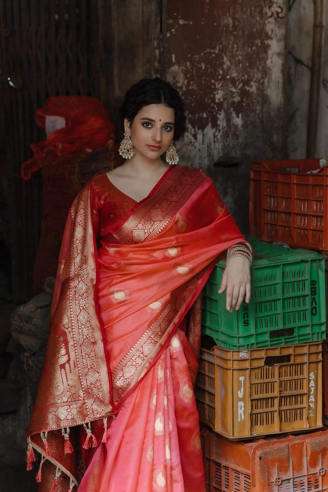 Full-length frame of the coral Banarasi, the pallu long, the model seated on stacked crates