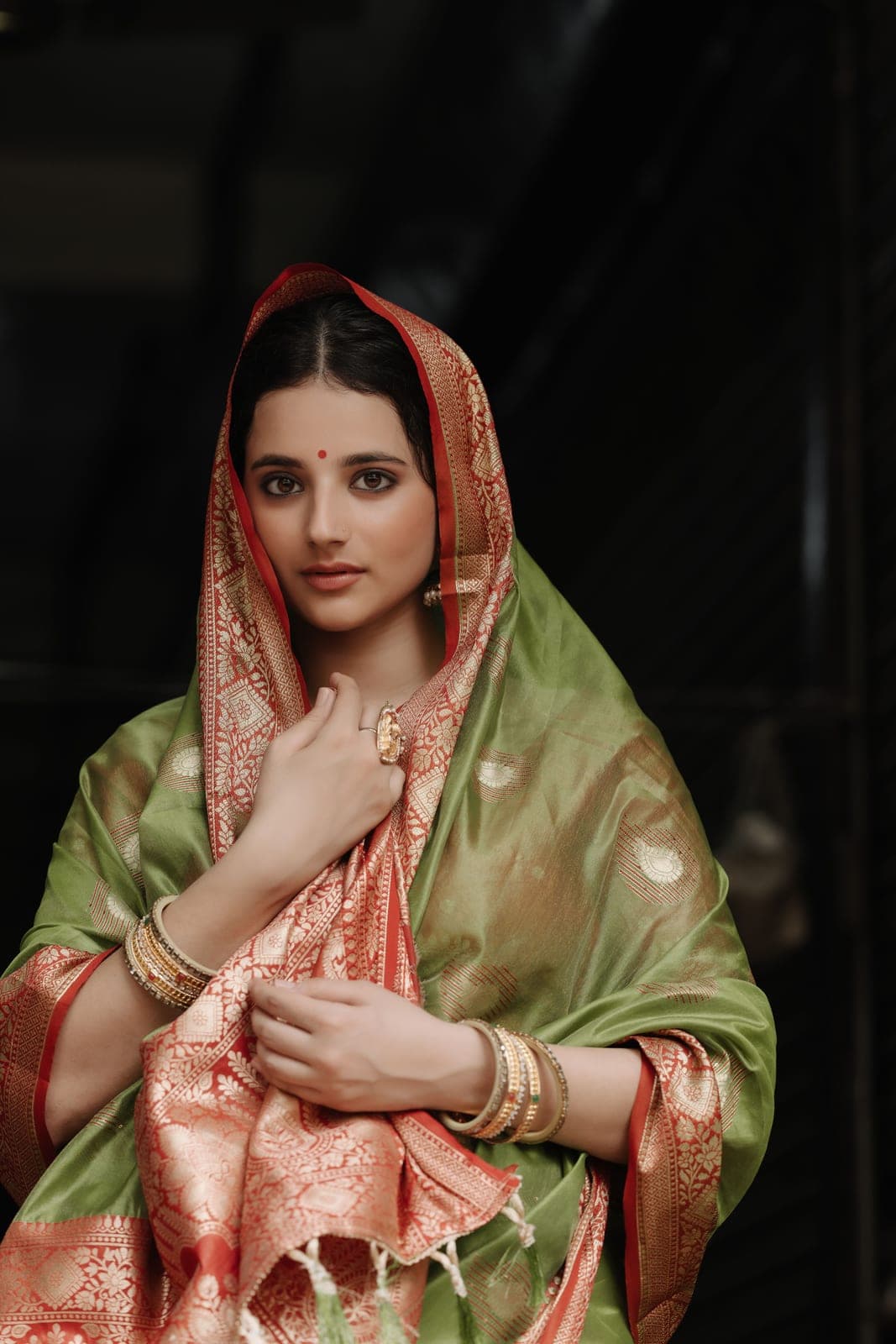 The model with a green Banarasi dupatta over her head, holding its gold border