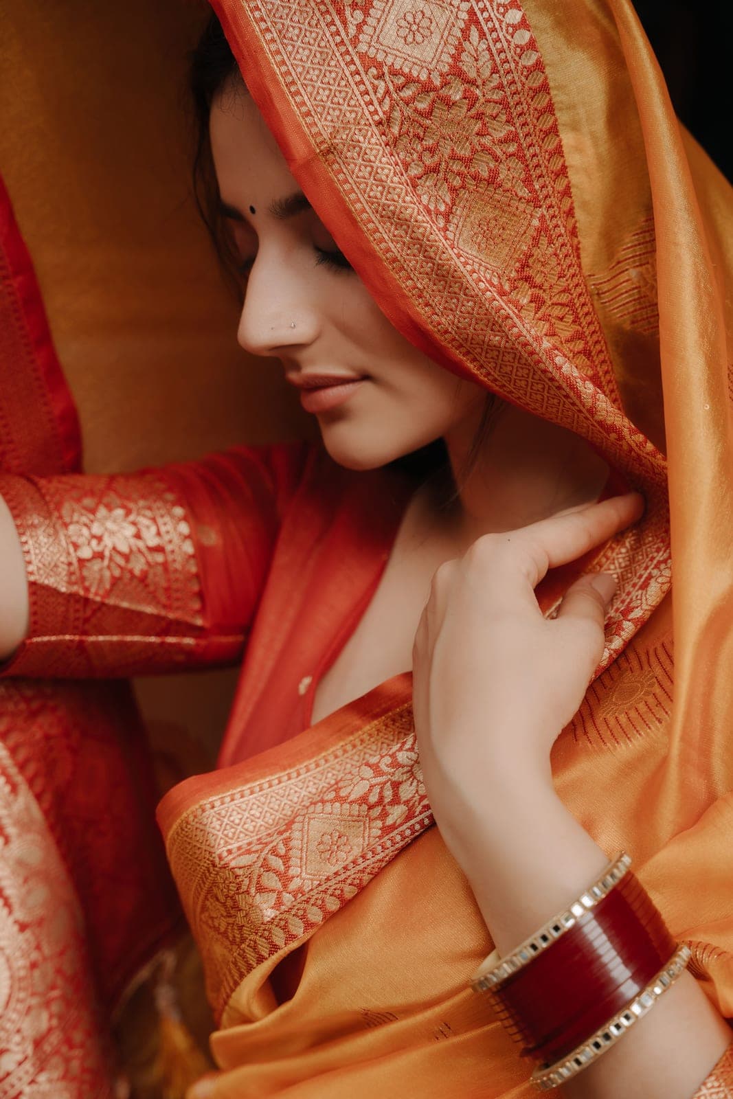 Close-up of saffron silk over coral, with red glass bangles on the wrist