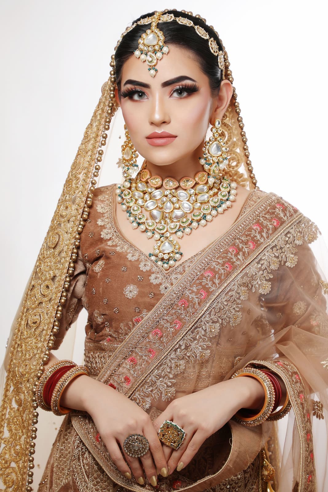 A bride in a kundan rani haar, matha patti and earrings, with a dupatta edged in gold