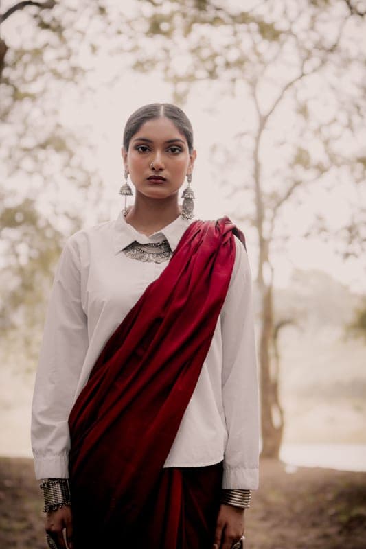 A model in a maroon saree draped over a white shirt, in a dry field