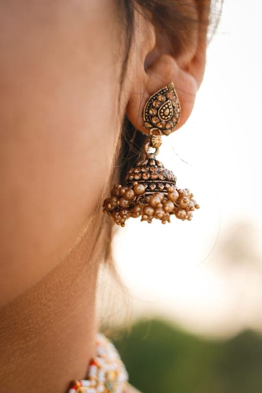 Close-up of a gold jhumka earring on an ear, the neck left clear