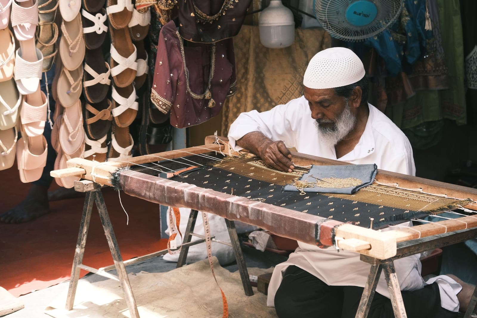 An embroiderer at a long wooden frame in a workshop, the cloth stretched tight
