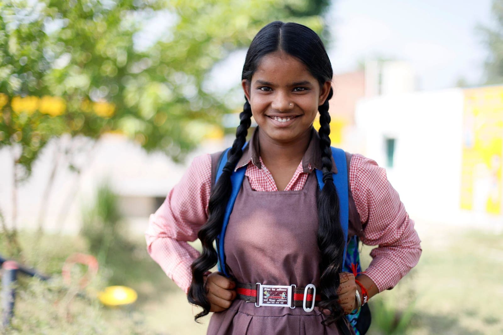 A smiling schoolgirl with long plaits and a school bag, outdoors