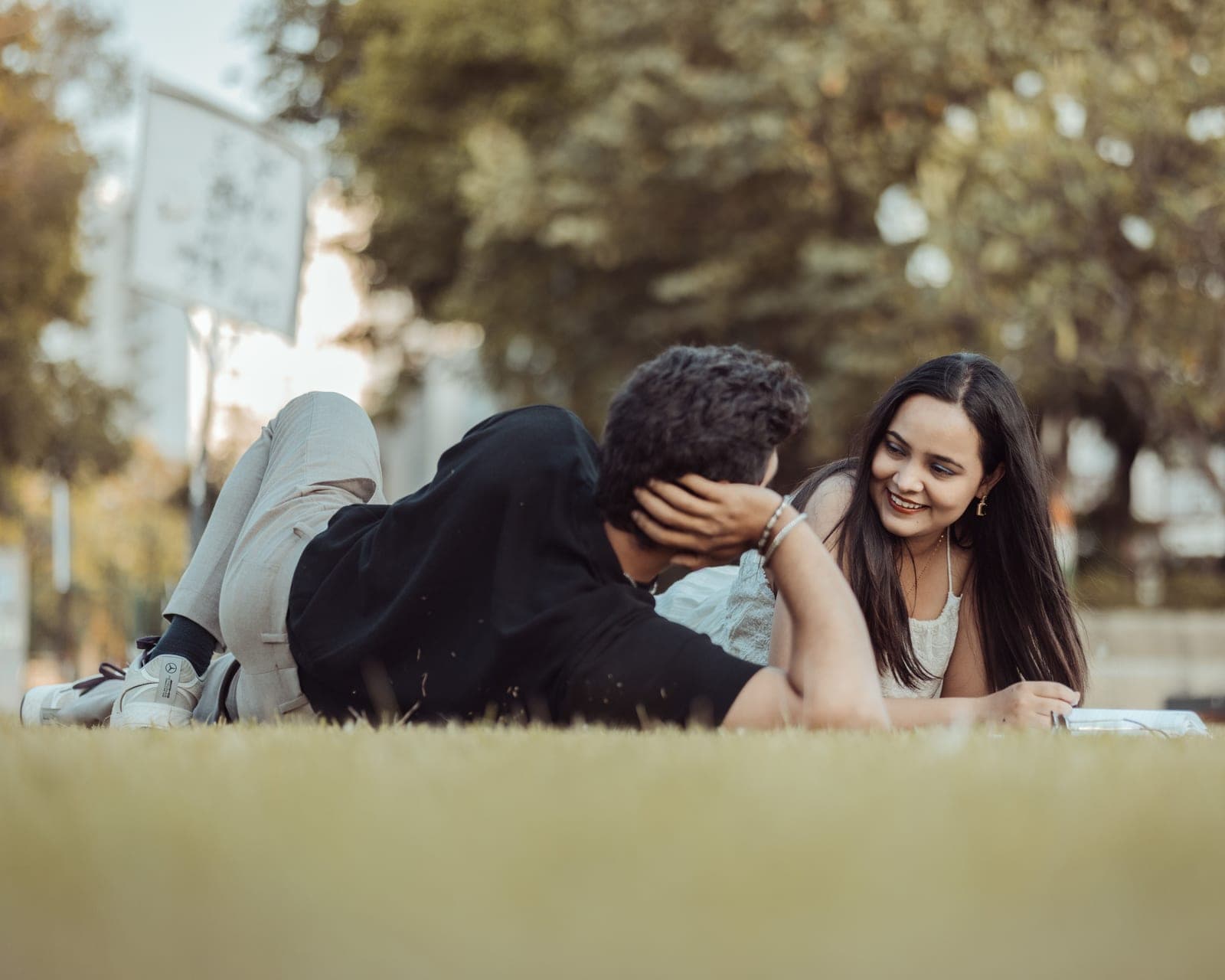 Arjun lies back on the grass with his eyes closed while Tanvi, propped on her elbows beside him, laughs