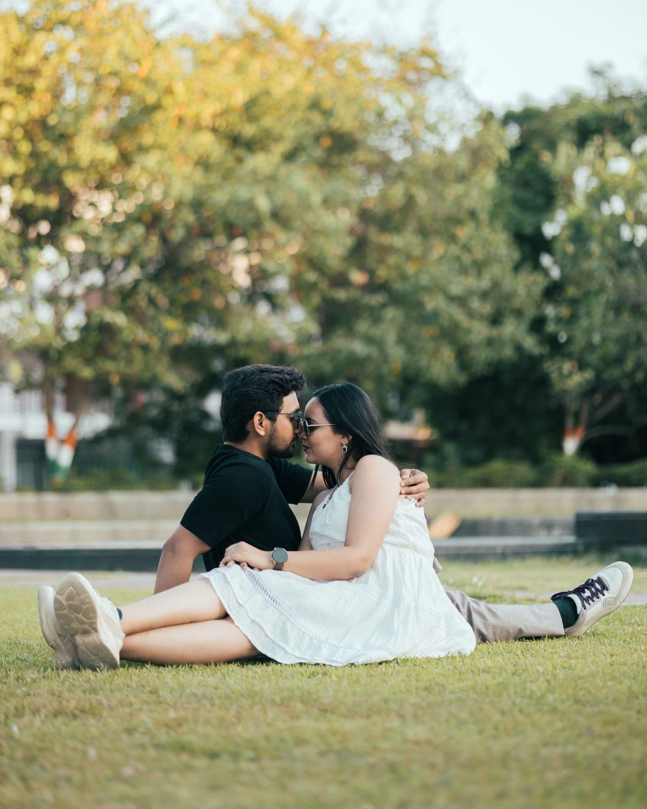 Tanvi and Arjun sit close together on a lawn, sharing a kiss