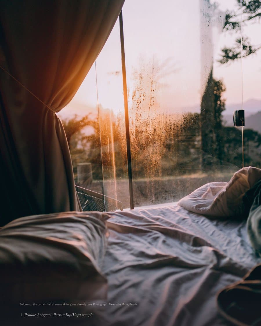 A bed by a window at first light, curtain half drawn